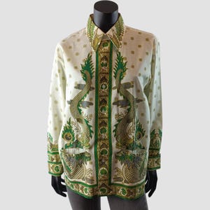 Op de afbeelding: Een off-white overhemd met lange mouwen en knoopsluiting, voorzien van een opvallend groen en goudkleurig drakenmotief op de voorpanden. Het kledingstuk heeft een puntige kraag, een centrale verticale strook met patronen en twee zakken.