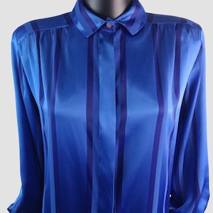 May include: A blue button-down shirt with vertical stripes in varying shades of blue. The long-sleeved shirt has a classic collar and is made of a shiny, silky material. The shirt is displayed on a mannequin.