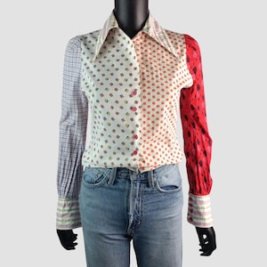 May include: A patchwork button-down shirt with a unique design. The shirt features a mix of patterns, including floral, polka dots, and plaid. The right sleeve is red with a black pattern. The shirt is paired with blue jeans.
