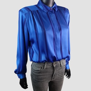 May include: A long-sleeved, blue satin blouse with vertical stripes in varying shades of blue. The blouse features a collared neckline and buttoned cuffs. The garment is displayed on a mannequin.