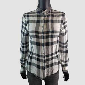 May include: A long-sleeved button-down shirt in a black and white plaid pattern. The shirt has a classic collar and buttoned cuffs. The fabric appears to be lightweight, suitable for layering or warmer weather.