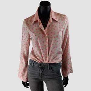 Peut inclure: Une chemise rose à boutons avec un motif floral de petites fleurs roses et vertes. La chemise à manches longues a un col et est associée à un jean en denim gris.