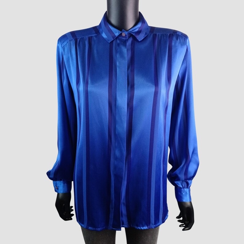 May include: A long-sleeved blue shirt with vertical stripes in varying shades of blue. The shirt has a classic collar and buttoned cuffs. The fabric appears to be a shiny satin or silk.