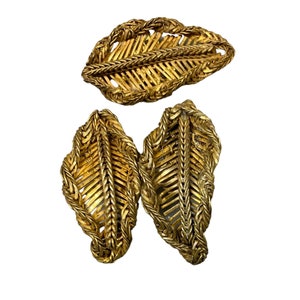 Peut inclure: Un ensemble de trois broches en forme de feuille dorées. Les broches sont en métal tissé et présentent un design délicat et complexe.