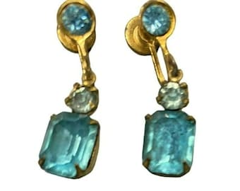 Könnte beinhalten: Ein Paar goldfarbene Ohrclips mit blauen und klaren Glassteinen. Die Ohrringe haben einen rechteckigen blauen Stein mit einem kleineren klaren Stein darüber.