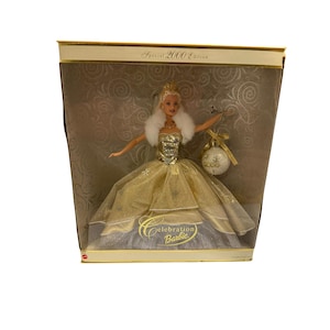 May include: A Special 2000 Edition Celebration Barbie doll in a gold and silver gown, holding a decorative ornament. The doll is in its original box with a gold and cream color scheme.