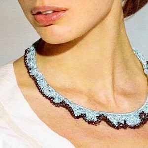 May include: A light blue crocheted necklace with a scalloped edge and dark brown beads. The necklace is worn around the neck and is a delicate piece of jewelry.