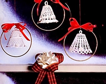 May include: Three white crocheted bell ornaments with red bows hanging from gold hoops. The ornaments are displayed on a white surface with a red and black plaid bow.