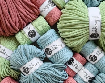 May include: Close-up of various spools of cotton rope in shades of green, blue, and pink. Each spool is labeled with the brand name "Bobbiny".