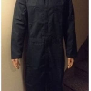 May include: A full-body Halloween costume featuring a white mask with black eye holes and a dark navy blue jumpsuit. The costume includes black shoes and a brown wig. The mask is a prominent feature, with a blank, expressionless face.