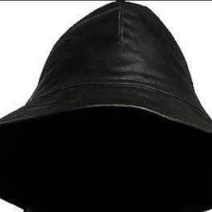 Puede incluir: Un sombrero de pescador de cuero negro con ala ancha. El sombrero tiene una copa redondeada y un ala estructurada. El sombrero está hecho de un material de cuero liso y brillante. El sombrero es de color negro liso.