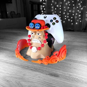 Peut inclure: Une figurine imprim&eacute;e en 3D d'un personnage de dessin anim&eacute; avec un chapeau de paille, des perles rouges et un cr&acirc;ne blanc. La figurine tient une manette de jeu vid&eacute;o blanche.