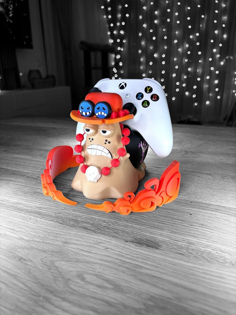 Peut inclure: Une figurine imprim&eacute;e en 3D d'un personnage de dessin anim&eacute; avec un chapeau de paille, des perles rouges et un cr&acirc;ne blanc. La figurine tient une manette de jeu vid&eacute;o blanche.