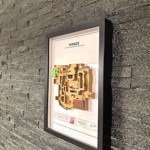 May include: A framed map of the Mirage map from the video game Counter-Strike: Global Offensive. The map is printed in brown and green on a white background. The frame is black and has a white mat.