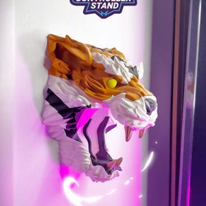 May include: A wall-mounted tiger head controller stand. The tiger head is orange, white, and black with yellow eyes and sharp teeth. The text "TIGER CONTROLLER STAND" is above the tiger head. The text "TIGER HEAD" is below the tiger head.