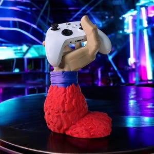 May include: A red, textured hand holding a white video game controller. The hand is wearing a purple and blue wristband.