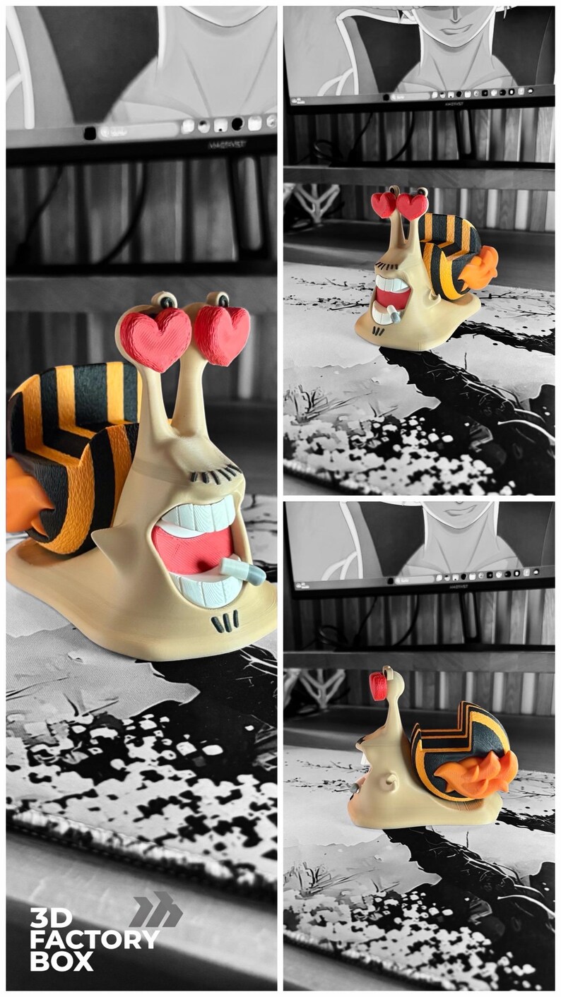 May include: A whimsical 3D-printed snail figurine with a beige body, a striped shell, and heart-shaped eyes. The snail has an open mouth with visible teeth and a small object. The figurine is set against a black and white background. The text "3D FACTORY BOX" is visible.