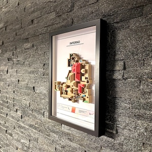 May include: A framed map of the "Inferno" map from the video game Counter-Strike: Global Offensive. The map is printed in black and white with red accents. The frame is black and the map is mounted on a white background.