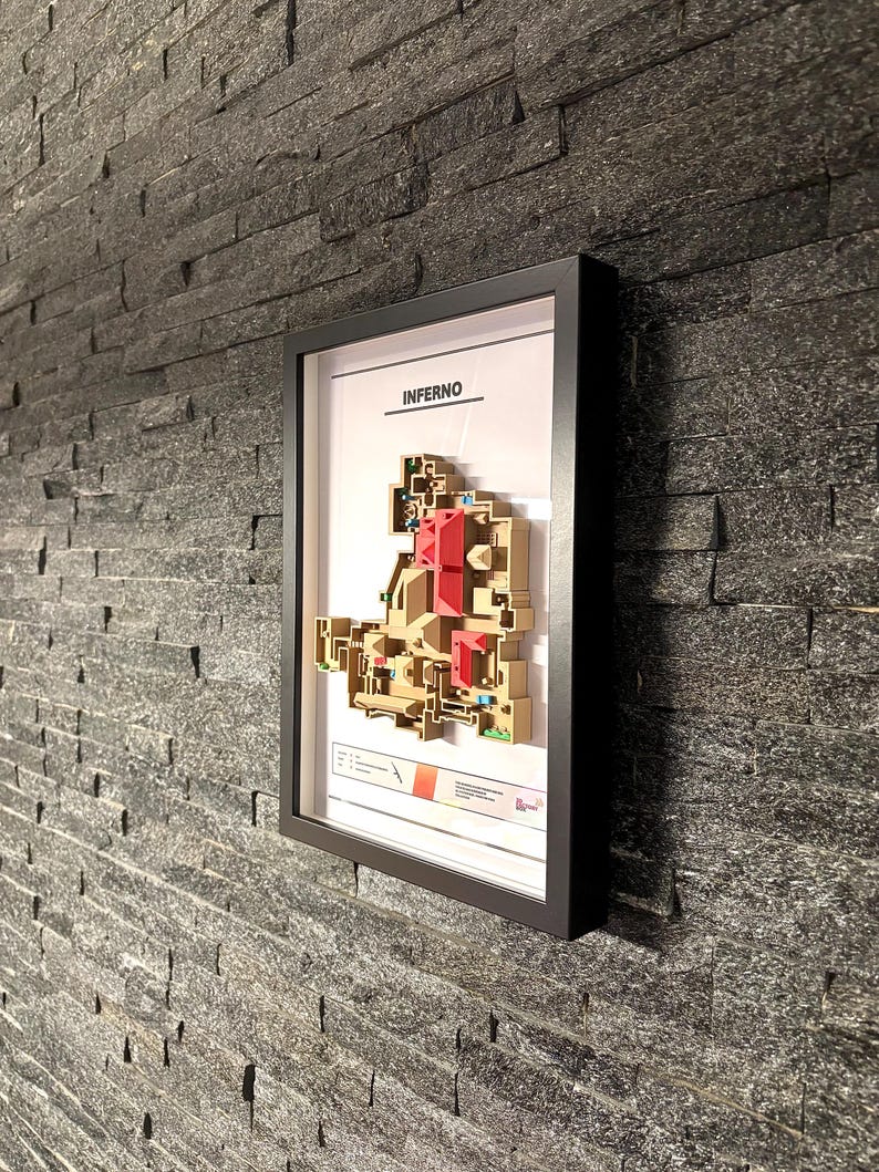 May include: A framed map of the "Inferno" map from the video game Counter-Strike: Global Offensive. The map is printed in black and white with red accents. The frame is black and the map is mounted on a white background.