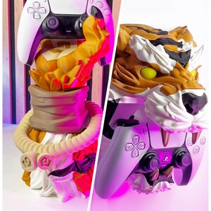 May include: A white and black PlayStation 5 controller rests on a decorative tiger head stand. The stand features a detailed tiger head with orange, brown, and white fur, and yellow eyes. The stand has a beige rope-like design.
