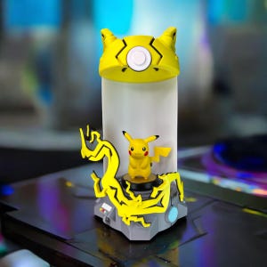 May include: A yellow Pikachu figurine with a yellow and black lightning bolt base. The base has a white light inside. The figurine is on a gray surface.