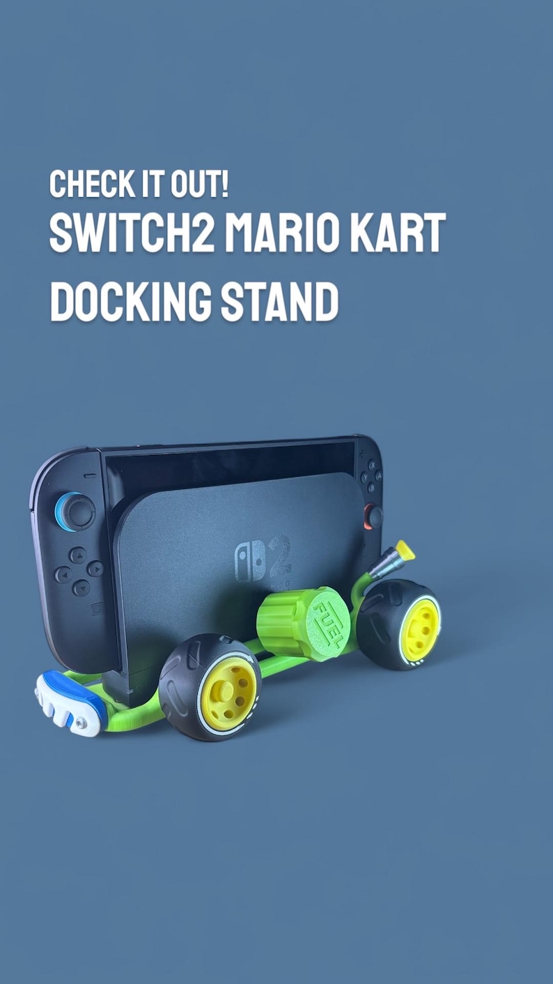 K&ouml;nnte beinhalten: Ein schwarzer Switch2 Mario Kart Docking-St&auml;nder mit einem gr&uuml;n-gelben Kart-Design. Der St&auml;nder tr&auml;gt den Text "CHECK IT OUT! SWITCH2 MARIO KART DOCKING STAND". Der Kart hat schwarze R&auml;der mit gelben Zentren.