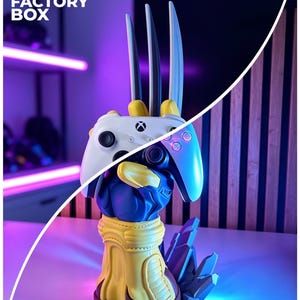 May include: A 3D printed controller stand shaped like a blue and yellow gloved hand with three long silver claws extending upward. The hand holds a white Xbox wireless controller. The base features jagged, crystalline rock-like structures.