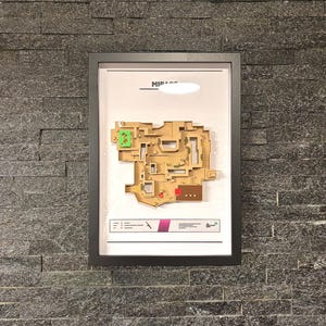 May include: A framed map of the Mirage map from the video game Valorant. The map is a 3D model with a beige and brown color scheme. The map is labeled "Mirage" at the top.