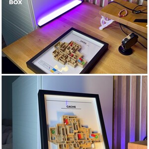 May include: A framed 3D model of a map labeled "CACHE" with a black frame. The model is beige with red and green accents, and is displayed on a wooden desk. The text "3D FACTORY BOX" is in the upper left corner.