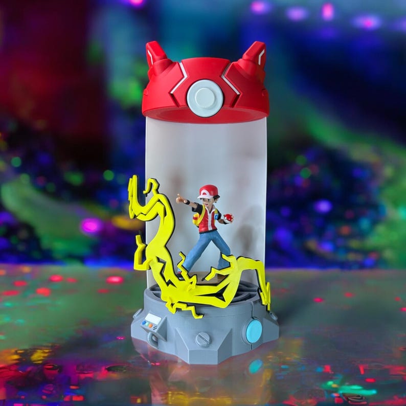 May include: A red and white Poke Ball shaped light-up figurine with a yellow lightning bolt design and a small red and white figure of a Pokemon trainer inside.