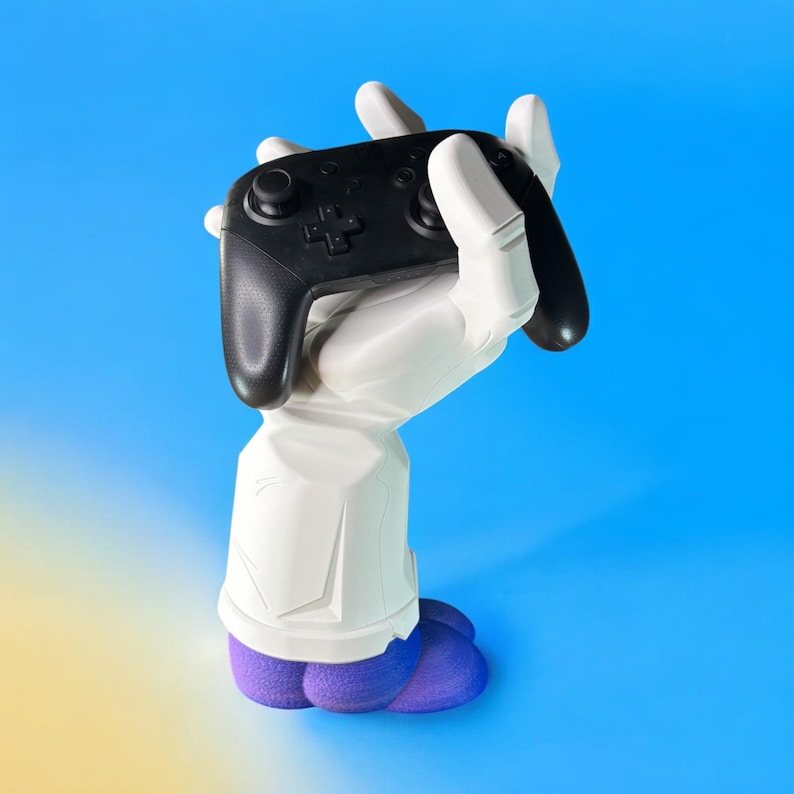 Puede incluir: Una figura de mano blanca sosteniendo un mando de videojuego negro. La mano lleva zapatos morados.