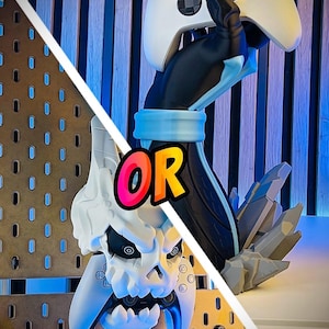 Peut inclure: Une manette Xbox blanche tenue par une main sculptée noire et bleue, avec un support en forme de crâne à gauche. Le mot "OR" est au centre, avec le texte "3D FACTORY BOX" en bas.