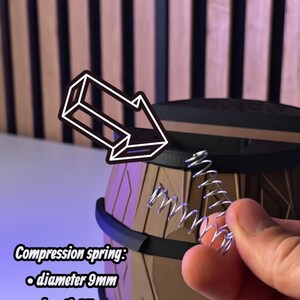 May include: Image shows a silver compression spring with a 9mm diameter, 35mm length, and 0.9mm strength. The text indicates it's for a sprint mechanism. The spring is held near a brown and black barrel-shaped object.