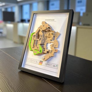 May include: Framed 3D map of the Overpass game level, featuring tan and green architectural details. The map is set against a white background within a black frame. The word "OVERPASS" is printed at the top.