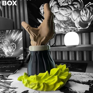 Op de afbeelding: Een 3D-geprinte sculptuur met een hand die uit een zwarte basis komt, met een geel, stekelig ontwerp. De achtergrond is zwart-wit, met de tekst "3D FACTORY BOX".