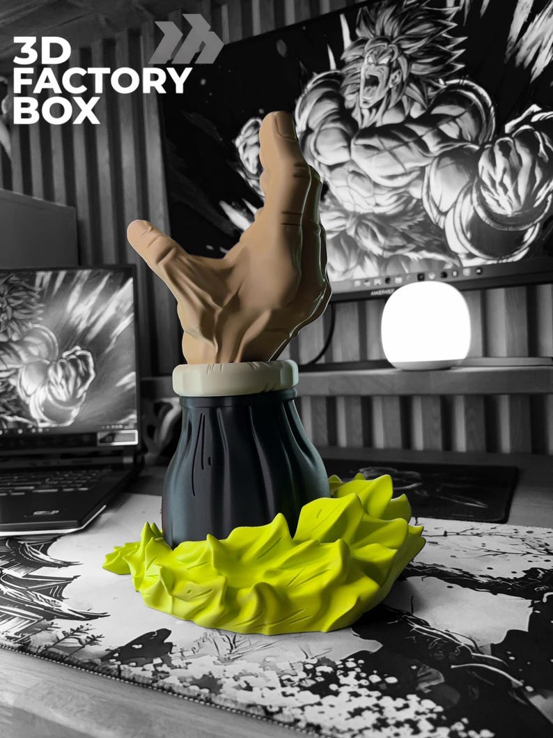 Op de afbeelding: Een 3D-geprinte sculptuur met een hand die uit een zwarte basis komt, met een geel, stekelig ontwerp. De achtergrond is zwart-wit, met de tekst "3D FACTORY BOX".