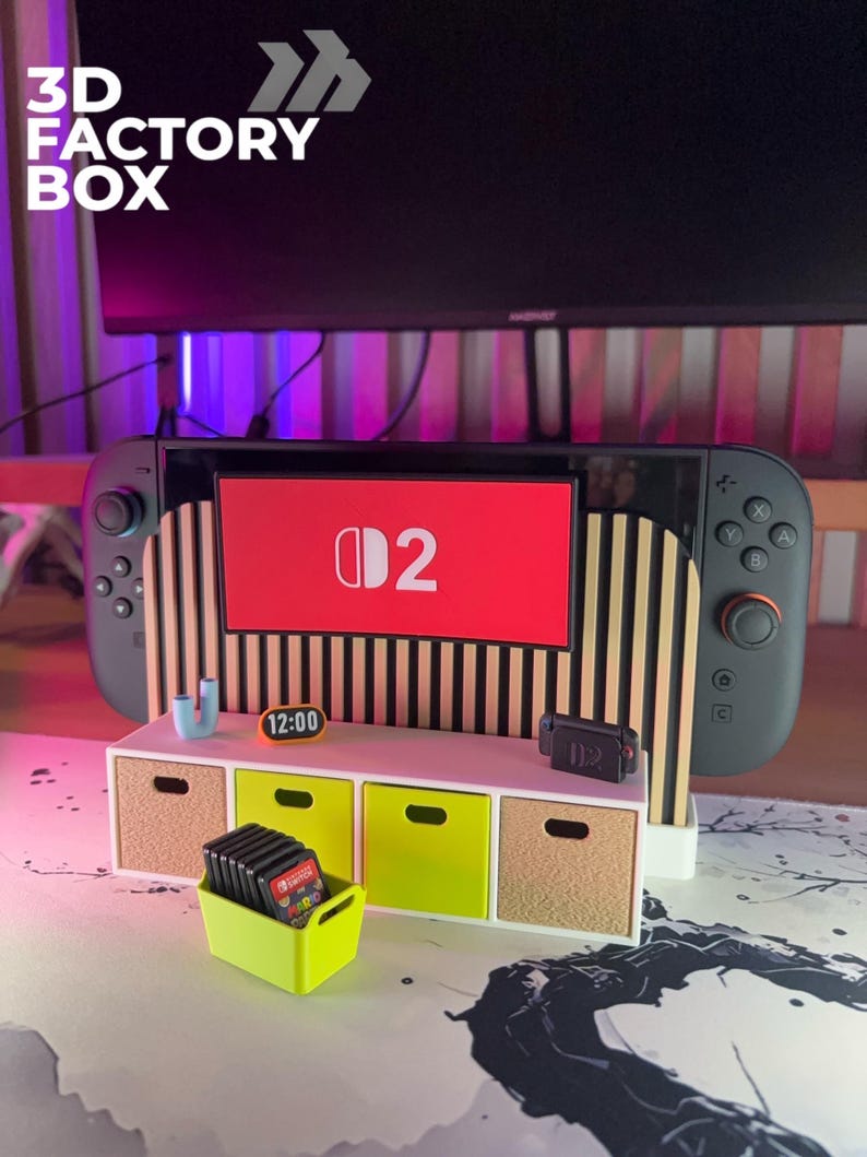 May include: A 3D Factory Box display featuring a Nintendo Switch console with a red screen displaying the "D2" logo. The display includes a small white cabinet with lime green and tan drawers, and a lime green container holding game cartridges. The time 12:00 is displayed.