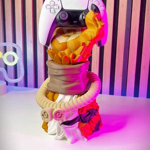 May include: A white and black PlayStation 5 controller stand with a tiger design. The stand has a detailed tiger head and body, with a white controller resting on top. The stand has the text "TIGER CONTROLLER STAND".