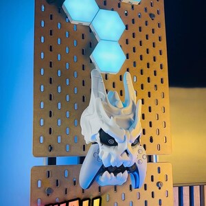 May include: A white skull-shaped wall mount with a video game controller, mounted on a pegboard. Above the skull are six blue hexagonal LED lights. The words "WALL MOUNTING!" are displayed in a colorful font.