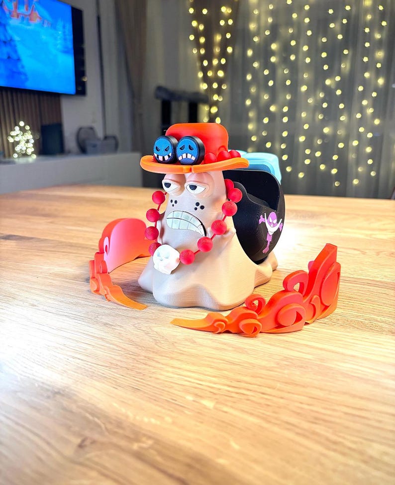 Peut inclure: Une figurine imprim&eacute;e en 3D d'un personnage de dessin anim&eacute; avec un chapeau rouge, des lunettes bleues et un collier de perles rouges. La figurine est debout sur une base avec des flammes orange.