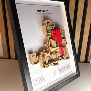 May include: A framed 3D map of the Inferno level from the video game "Dante's Inferno". The map is made of beige and brown plastic and features a red building in the center. The frame is black and the background is white. The title "Inferno" is printed at the top of the frame.
