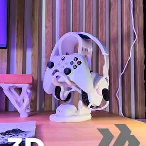 Könnte beinhalten: Ein weißer, 3D-gedruckter Ständer für Gaming-Headset und Controller. Der Ständer hält einen weißen Xbox-Controller und ein Paar Kopfhörer. Der Text "3D FACTORY BOX" ist unten im Bild zu sehen.