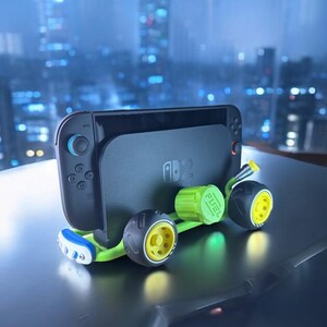 K&ouml;nnte beinhalten: Eine schwarze Nintendo Switch-Konsole mit blauen und roten Controllern ist an einem gr&uuml;nen und schwarzen Rennwagen-Zubeh&ouml;r befestigt. Das Auto hat gelbe und schwarze R&auml;der und das Wort "FUEL" ist auf dem gr&uuml;nen Tankdeckel aufgedruckt.