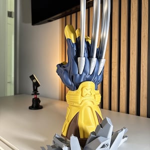 May include: A blue and yellow gauntlet featuring three long, silver-colored metallic claws extending from the knuckles. The gauntlet has a yellow wrist cuff with an X emblem and is mounted on a base of jagged, light gray crystalline structures.