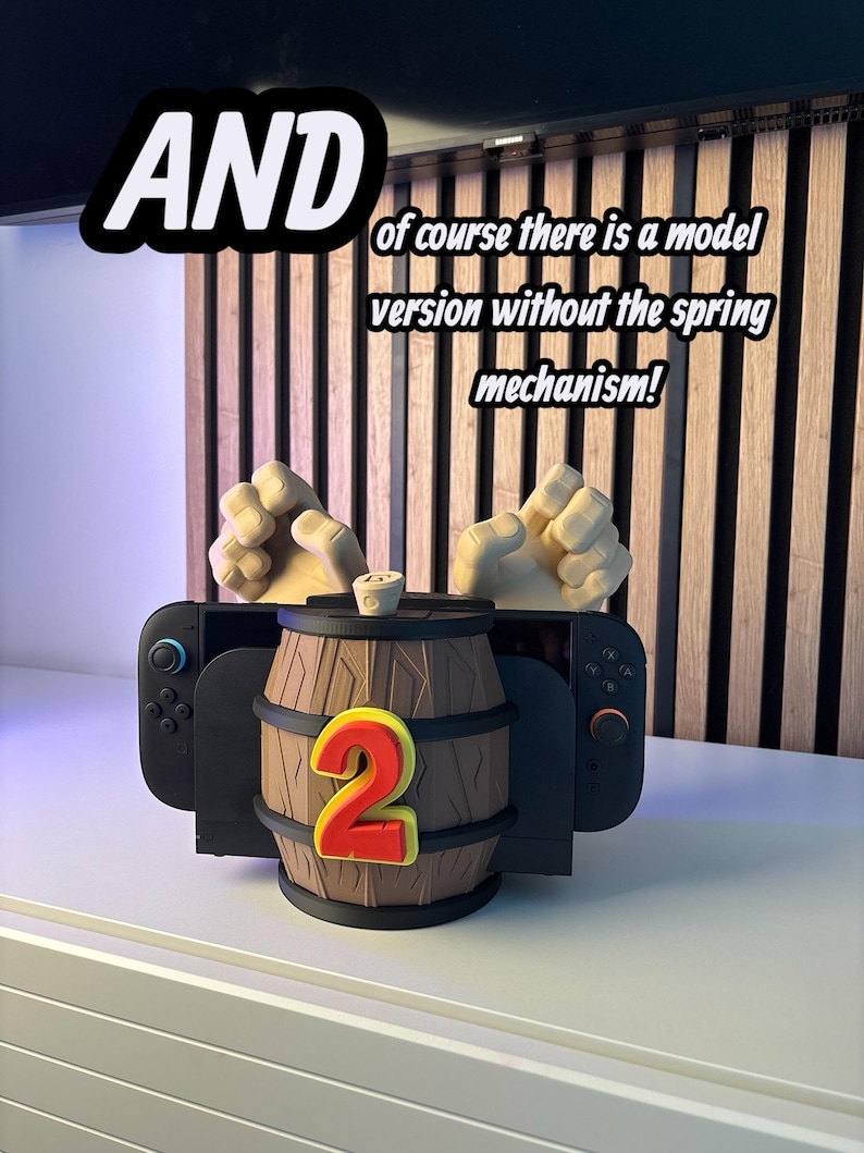 May include: A black Nintendo Switch controller holder shaped like a wooden barrel with a large red number 2. The text "AND" and "of course there is a model version without the spring mechanism!" are also visible.
