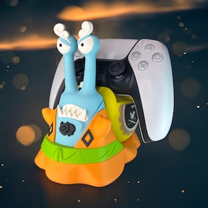 Könnte beinhalten: Eine blaue und orangefarbene Cartoon-Schnecke, die einen weißen und schwarzen Videospiel-Controller hält. Die Schnecke hat eine gelbe Schale und ein schwarzes Augenpflaster. Der Controller hat ein weißes Gesicht mit schwarzen Knöpfen.