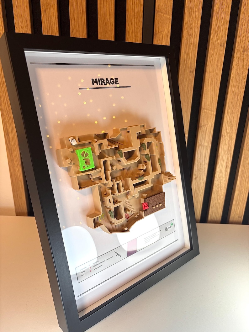 May include: A framed 3D map of the Mirage map from the video game Counter-Strike: Global Offensive. The map is made of beige plastic and is set against a white background. The frame is black and has the word "MIRAGE" printed in black at the top.