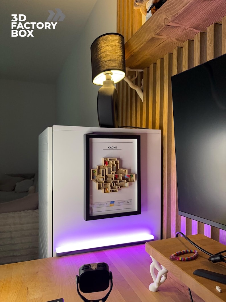 May include: A black table lamp with a cylindrical base and a black lampshade. The lamp sits atop a white cabinet, with a framed artwork and the text "CACHE" visible. The image also shows a wooden shelf and a desk.