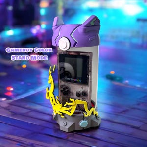 K&ouml;nnte beinhalten: Ein lila und grauer Game Boy Color-St&auml;nder mit einem gelben St&auml;nder und einem durchsichtigen Plastikgeh&auml;use. Der St&auml;nder tr&auml;gt den Schriftzug "GAME BOY COLOR". Der Text "GAMEBOY COLOR STAND MODE" ist auf dem Bild zu sehen.