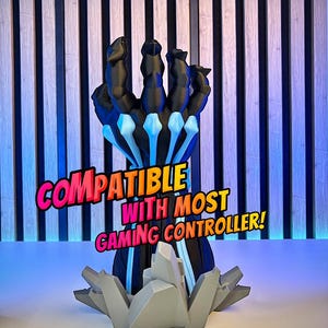 May include: A black and blue gaming controller stand shaped like a hand, with the text "COMPATIBLE WITH MOST GAMING CONTROLLER!" in pink and yellow. The stand has a gray base with the text "3D FACTORY BOX".